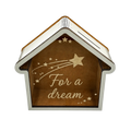 House-shaped wooden savings box with a transparent front panel, coin slot, white frame, star decorations, and “For a dream” engraving.